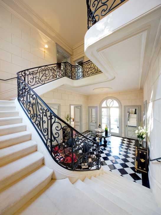 Grand staircase with ornate wrought-iron railings and black-and-white checkered floor in an elegant hotel entrance hall.