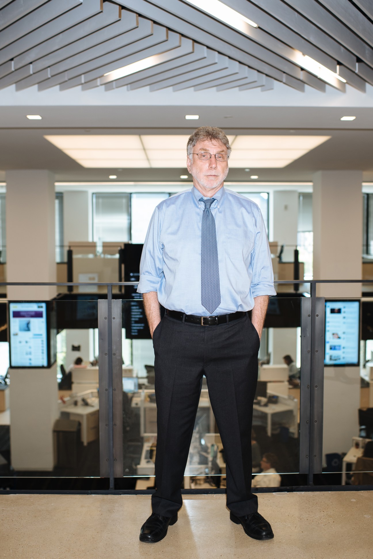 Marty Baron, executive editor of The Washington Post, stands in the newsroom wearing a light blue shirt and tie.