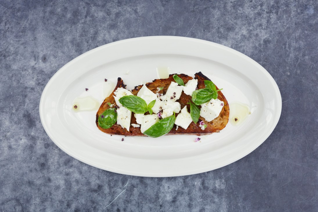 Goats' cheese bruschetta on white plate with basil and thyme garnish.