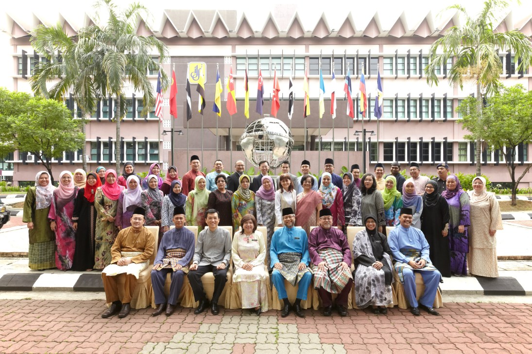 Group photo of Malaysian diplomacy students and faculty posed in front of a government building with international flags and a globe sculpture.