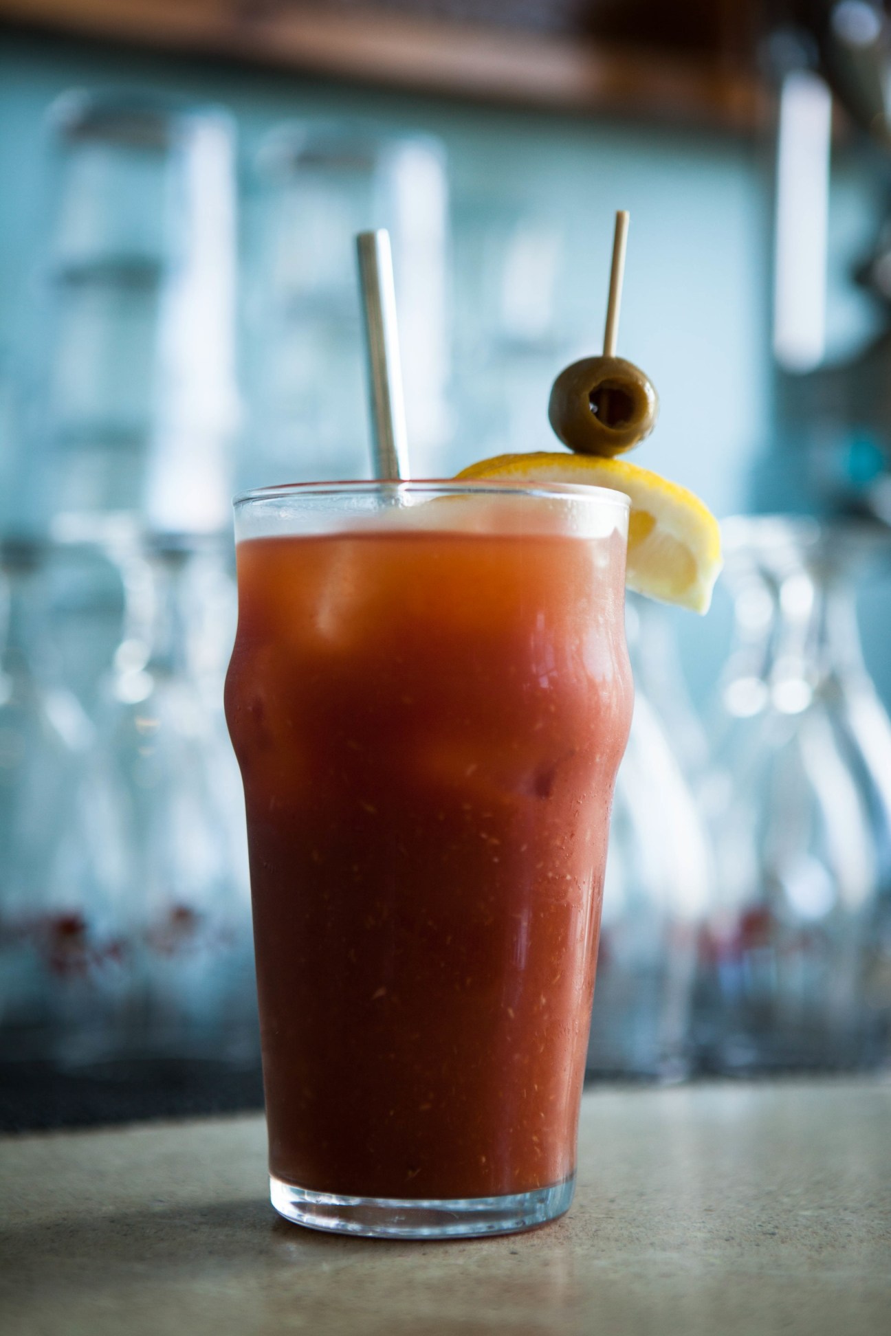 A Bloody Maria cocktail garnished with an olive and lemon slice, served over ice with a straw.