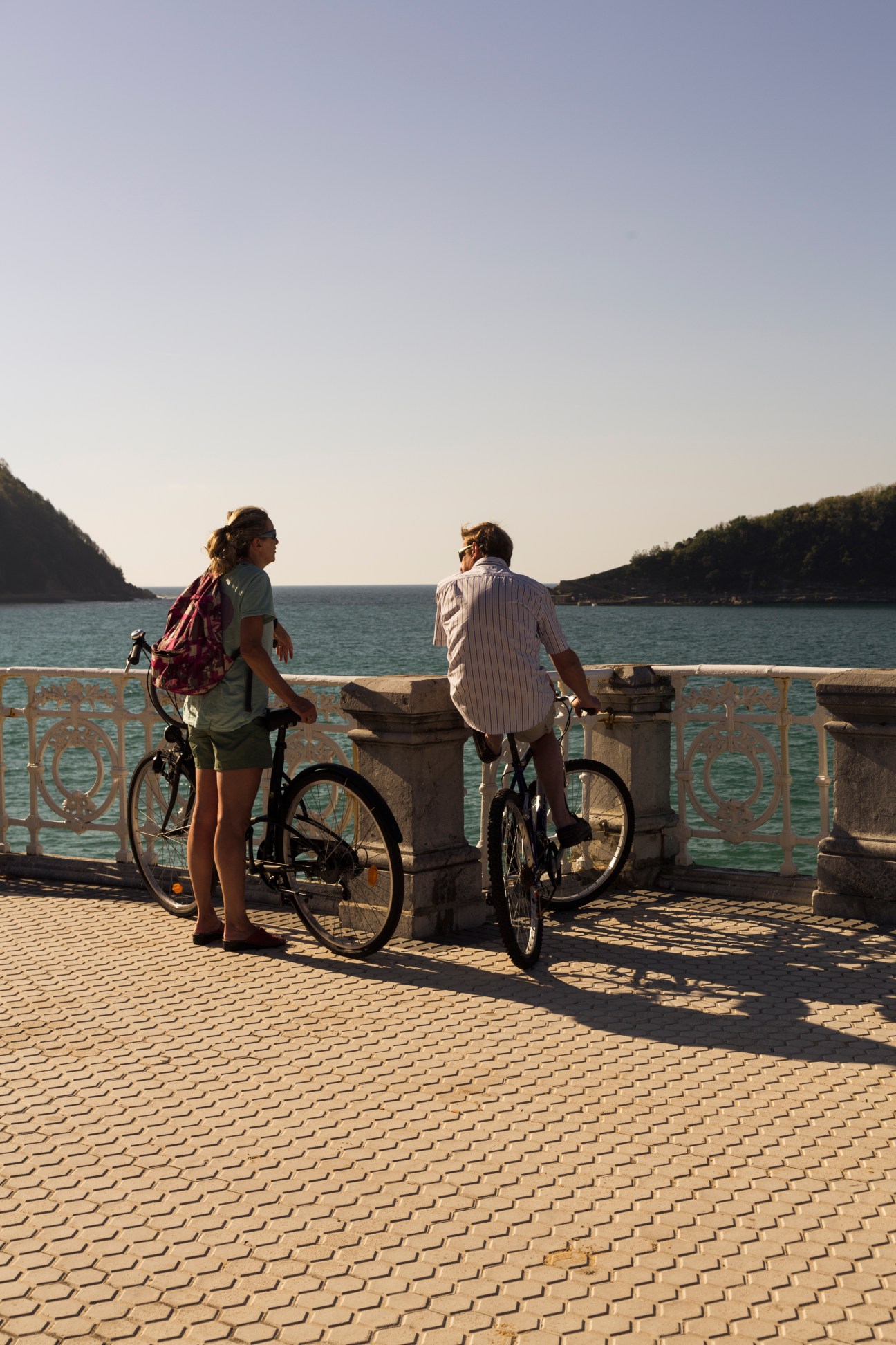 Two cyclists stop on Admiralbrücke bridge in Berlin to chat, leaning against the decorative stone railing overlooking the Landwehr canal.