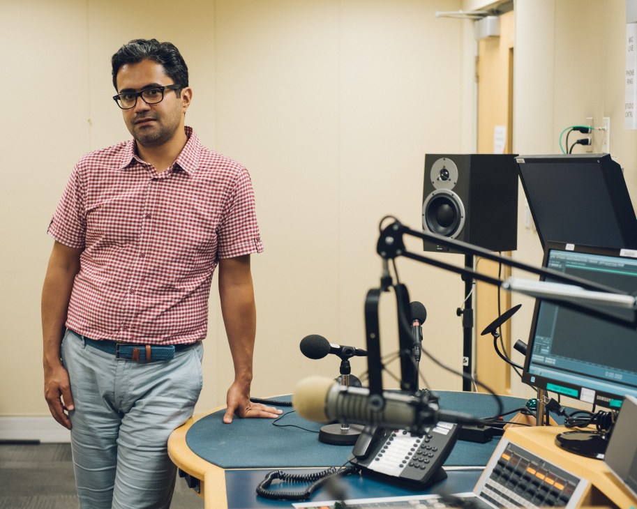 Hadi Nili, BBC Persian correspondent, stands in a radio studio beside broadcasting equipment.
