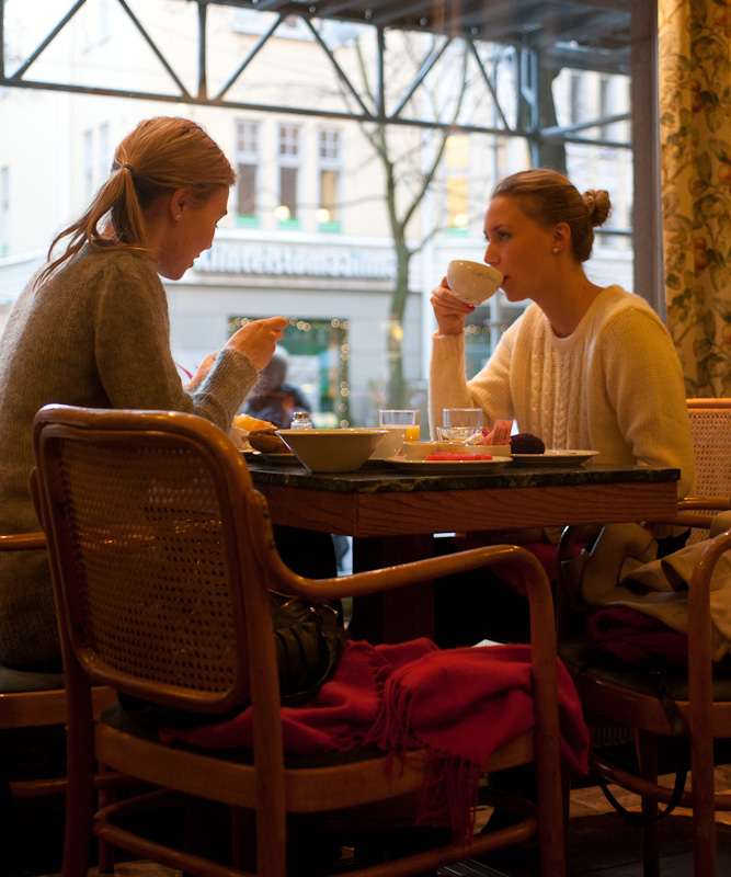 Two women sit at a table by a large window in Café Ekberg, eating pastries and drinking coffee.