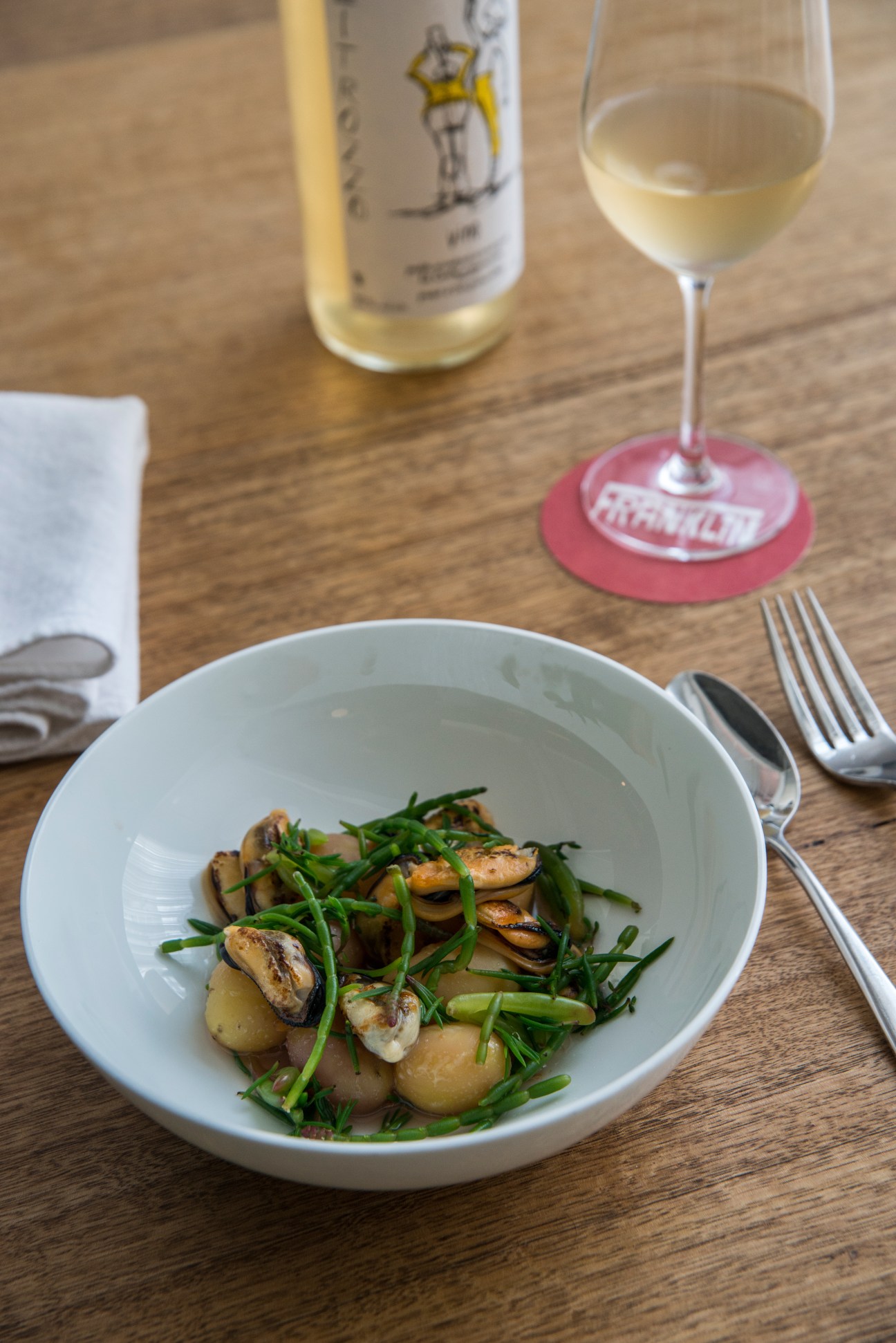 Mussels with new potatoes and samphire in a white bowl at Franklin restaurant, Hobart, with wine and place setting.