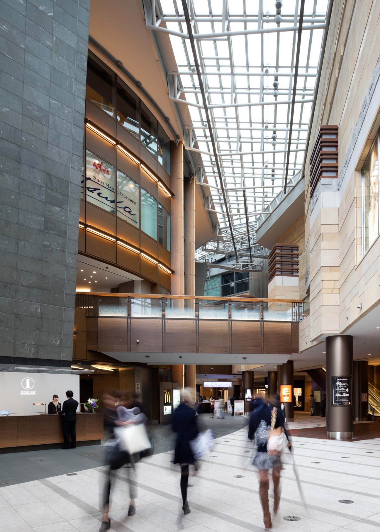 Interior of Roppongi Hills shopping center with glass ceiling, modern architecture, and people walking through the atrium.