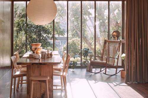 In Bed retail store in Sydney with wooden dining table, chairs, pendant light, and floor-to-ceiling windows overlooking greenery.