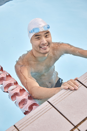 A swimmer in goggles and white swim cap smiles at the edge of North Sydney Olympic Pool.