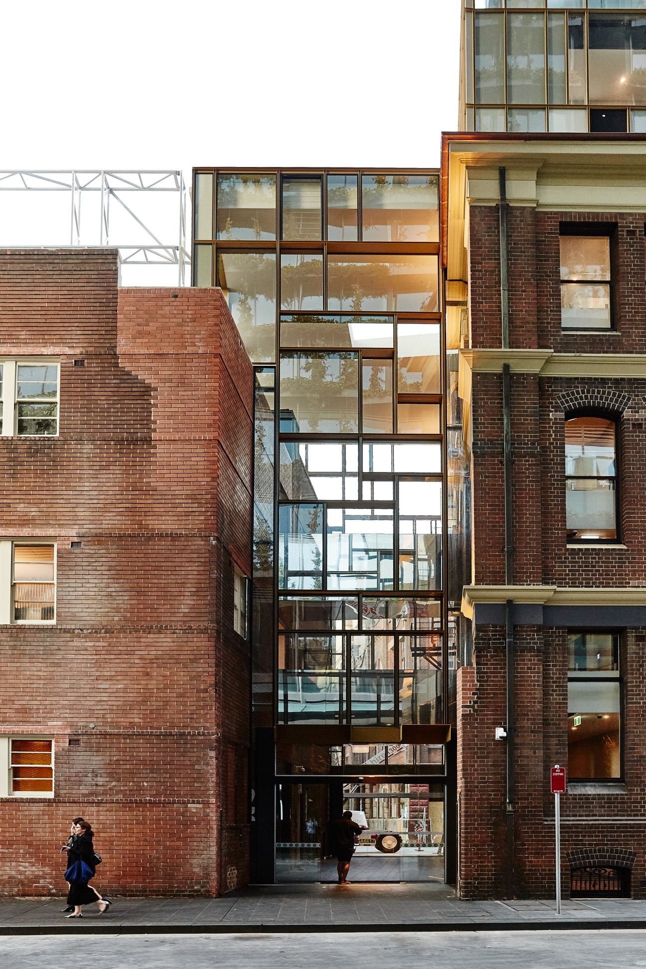 Modern glass and steel facade inserted between historic red brick buildings on a city street.