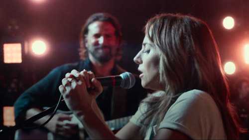Lady Gaga performs with a microphone while Bradley Cooper watches in A Star is Born.