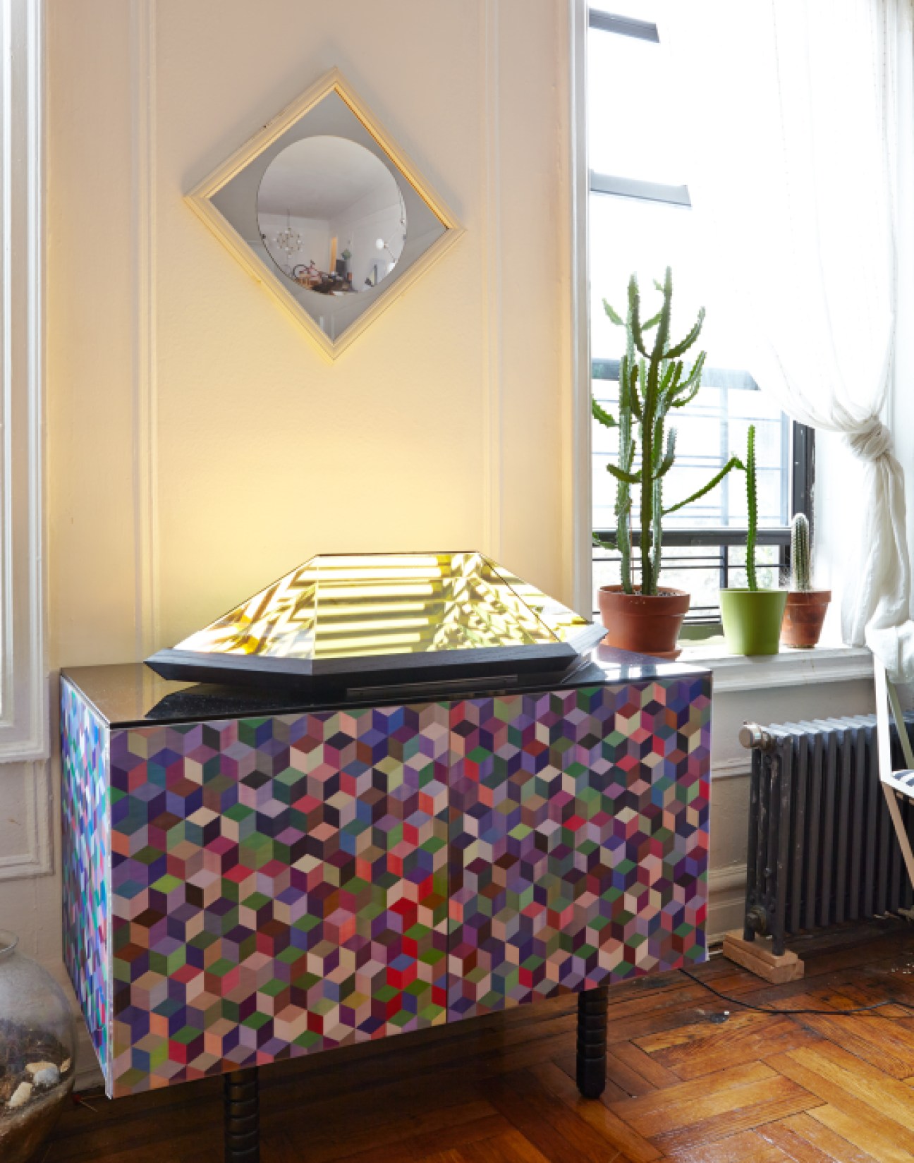 A geometric patterned table displays a gold pyramidal light fixture in a bright studio space.