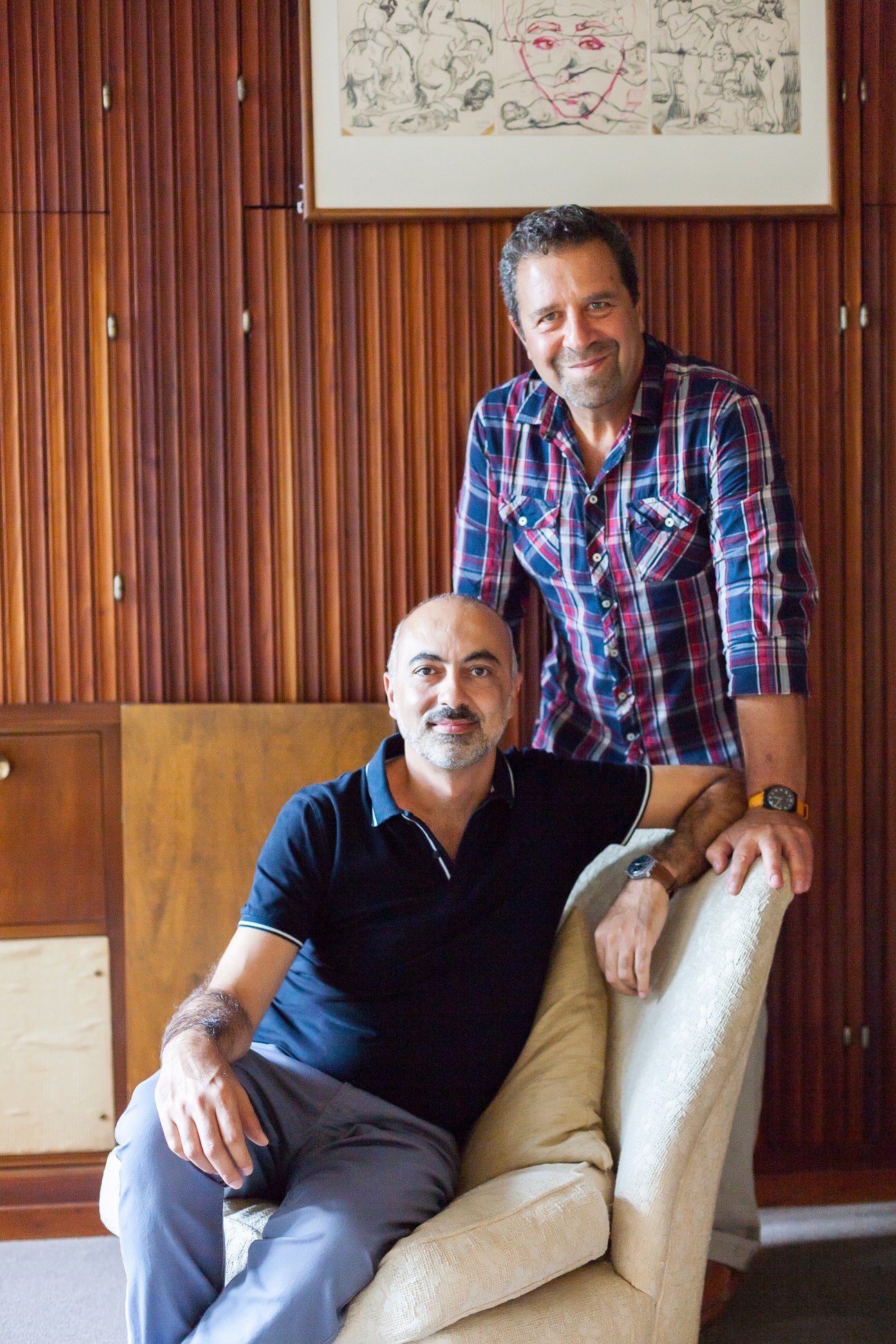 Gustavo Wagmaister and Salvo Tavella pose together in a wood-panelled apartment with modernist furnishings.