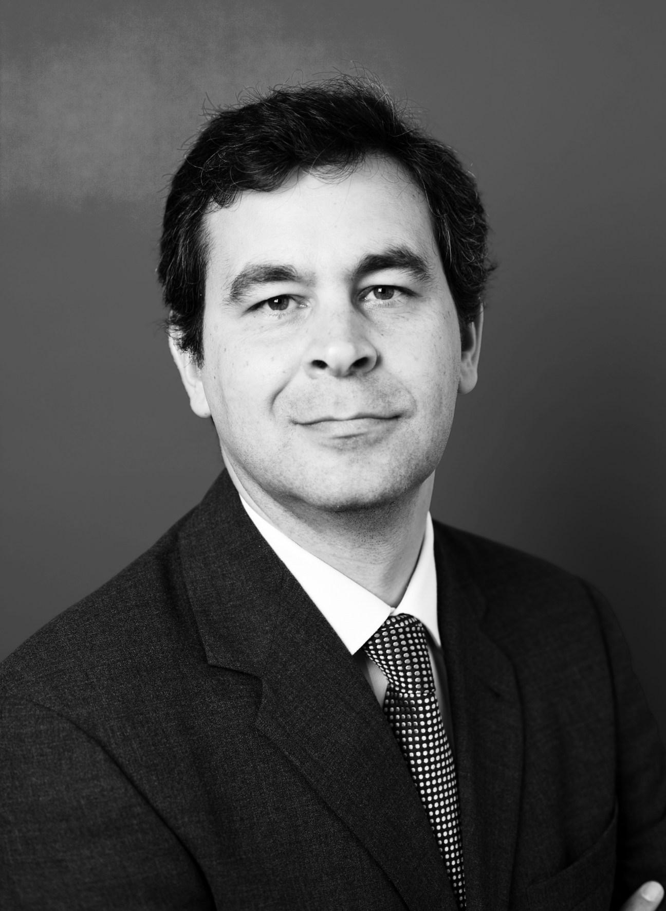 Black and white portrait photograph of a man in business attire with dark suit and patterned tie.