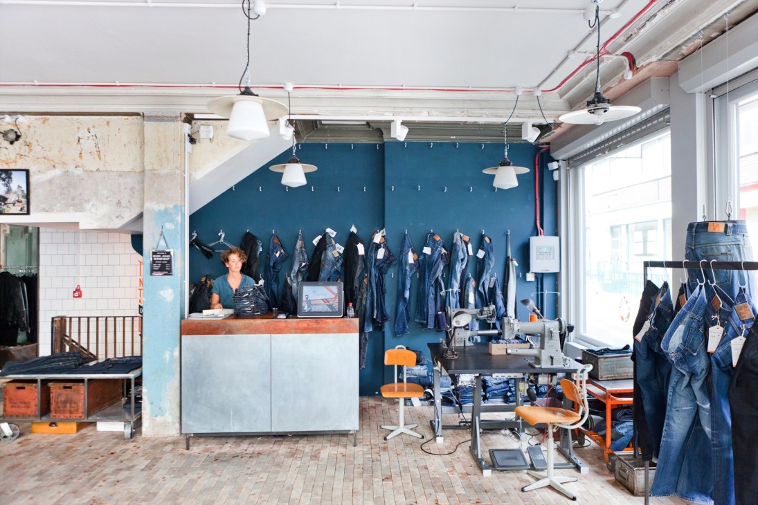 Interior of Nudie Jeans Repair Shop in London's Soho with denim displayed on blue wall and shop manager at counter.