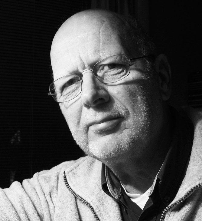 Black and white portrait of a man wearing glasses and a collared shirt with a sweater.