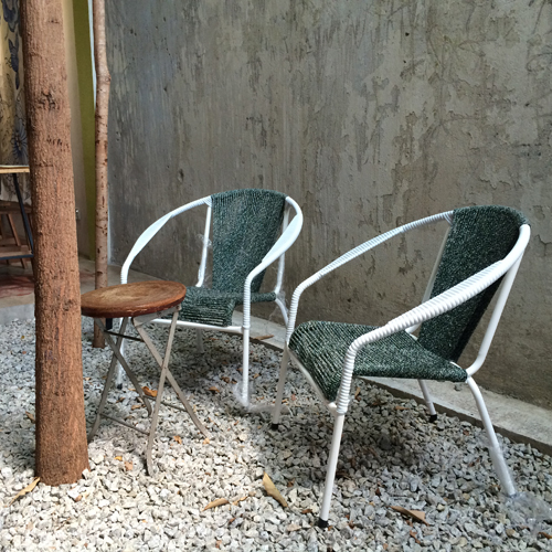 Two green woven rattan chairs with white metal frames positioned against a concrete wall.