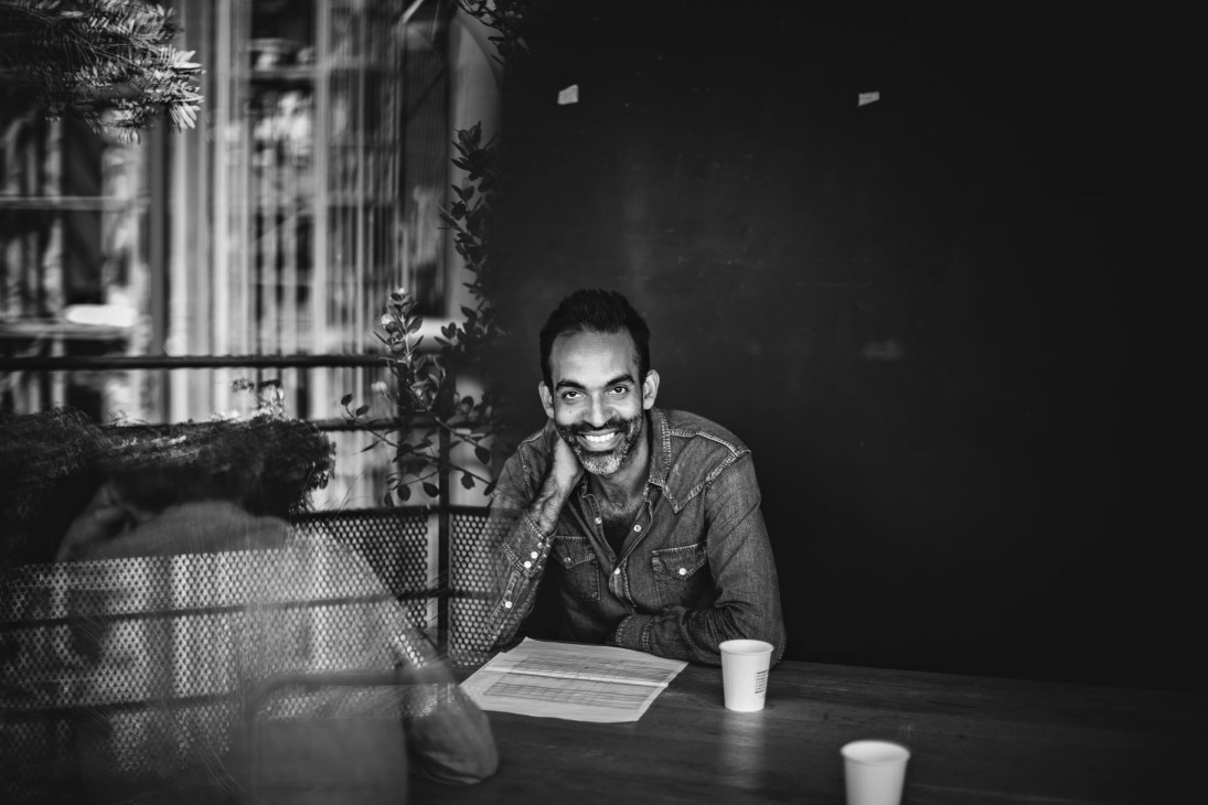 Man smiling at table with papers and coffee cups in black and white portrait.