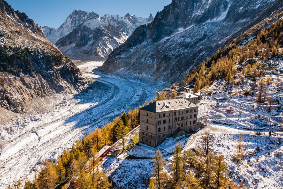 Historic stone hotel nestled in snow-covered Alpine valley with glacier and mountains in background.