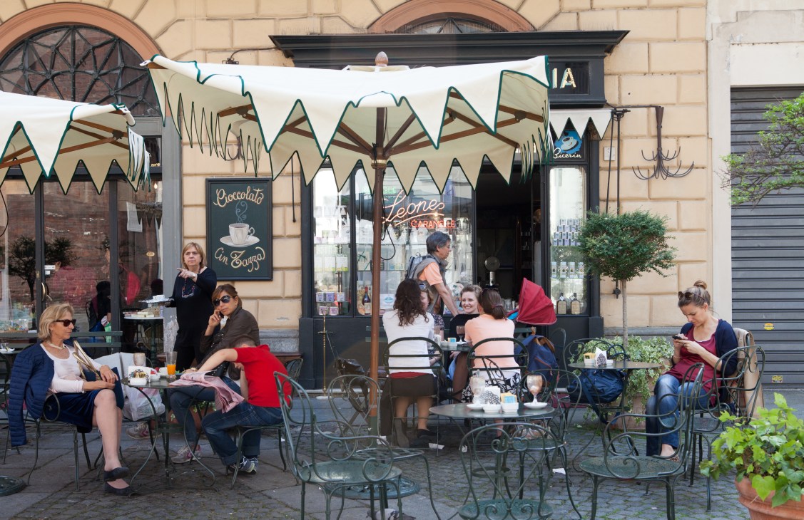 Bar Giornale's sunny terrace in Munich with guests seated under striped umbrellas at metal chairs.