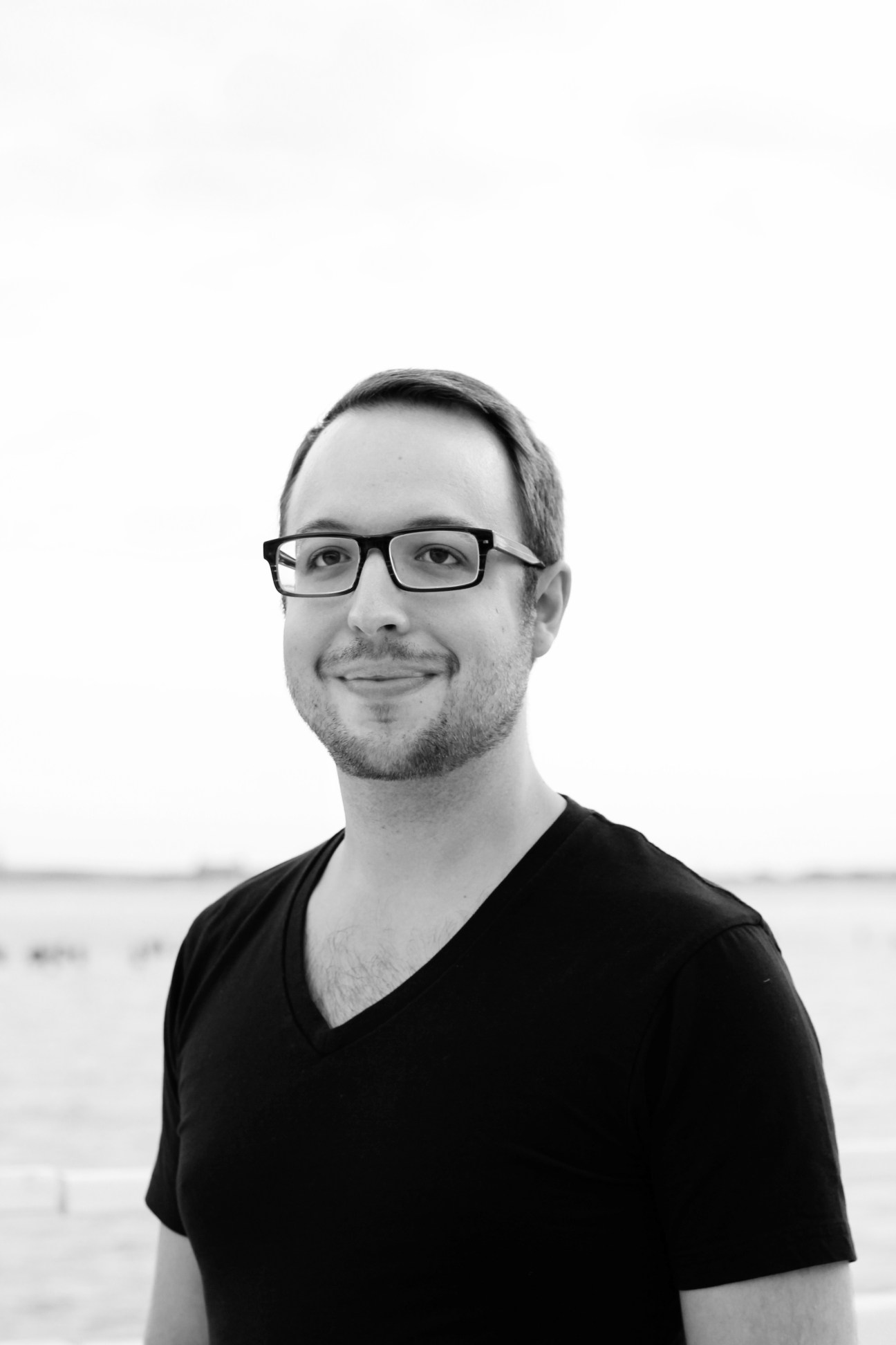 Black and white portrait of Caleb Kramer, editor in chief of Makeway, wearing glasses and a black v-neck shirt against a blurred background.
