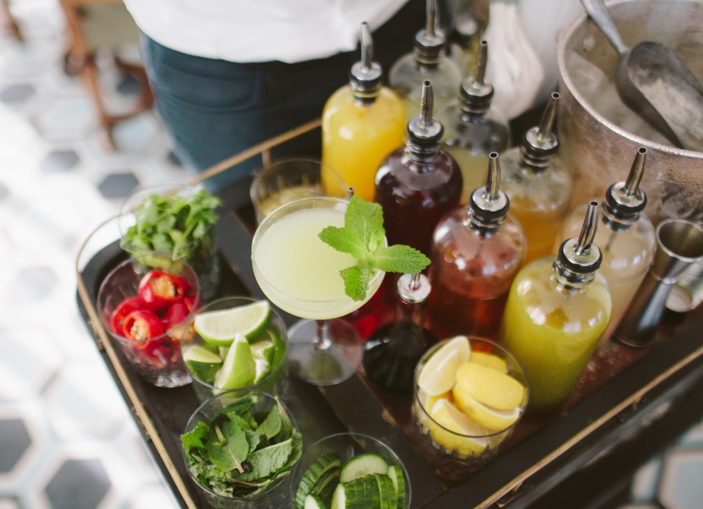 Overhead view of cocktail bar setup with bottles, fresh ingredients, and garnished drinks.