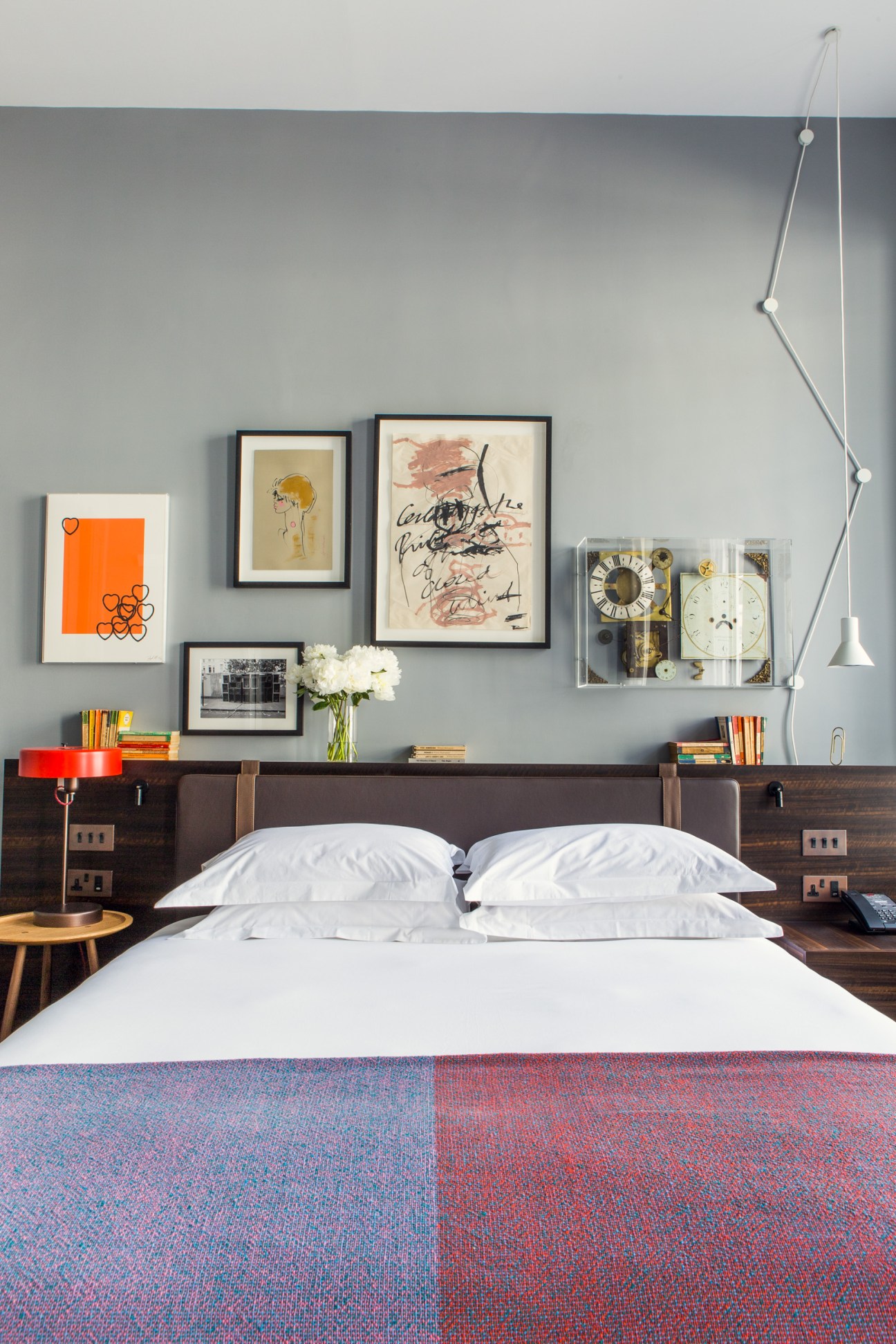 The Laslett hotel bedroom with contemporary art gallery wall, dark wood headboard, white bedding and pendant lighting.