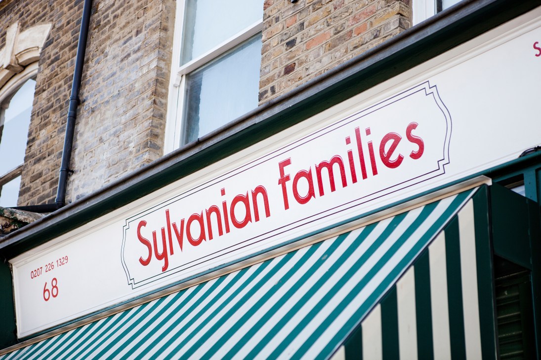 Hand-painted storefront sign reading 'Sylvanian Families' in red script on white background with decorative frame.