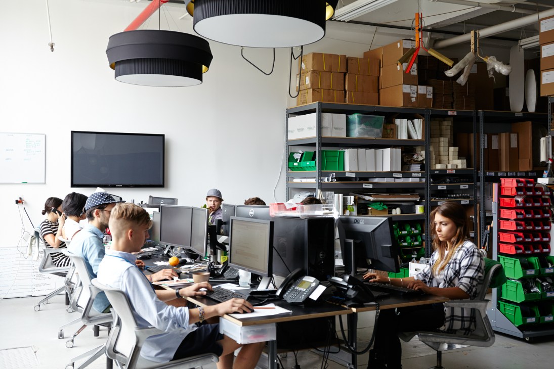 Rich Brilliant Willing studio workspace with employees at desks and shelving with materials and components.