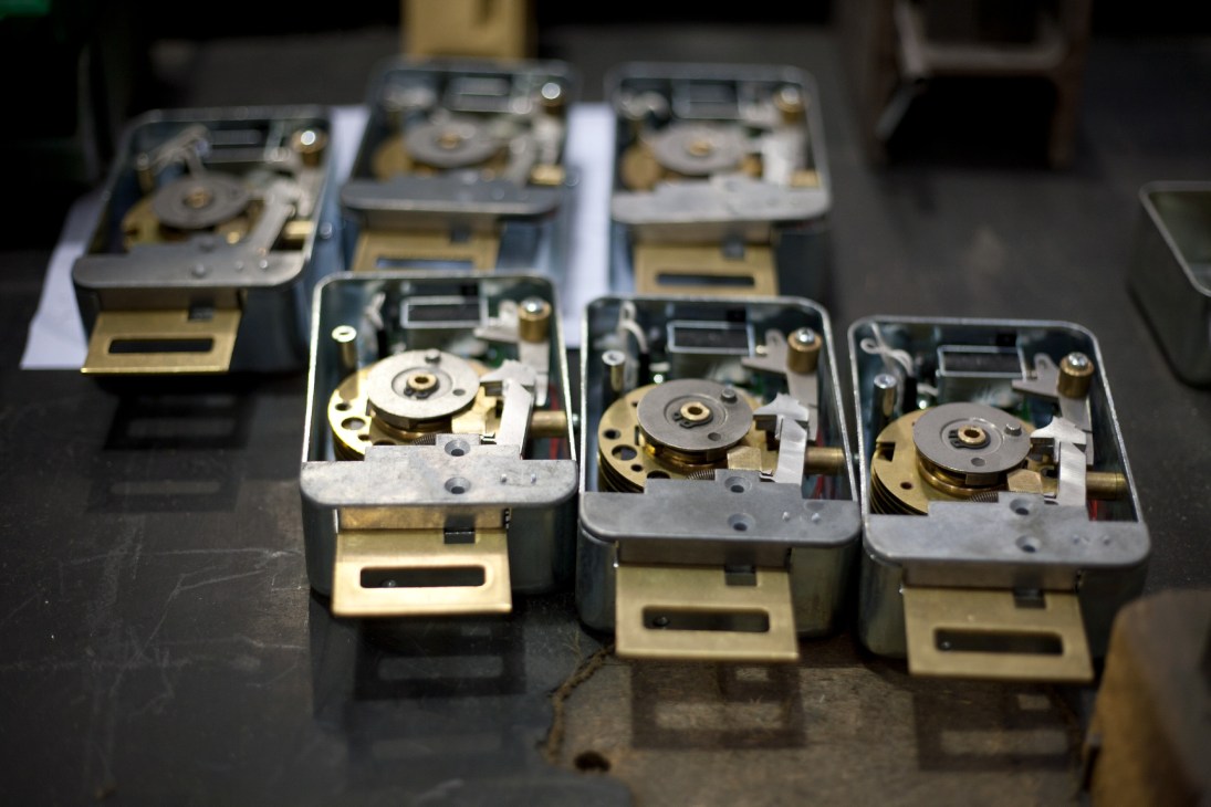 Steel keys, bronze mechanical combination locks and electronic keypads displayed on a work bench.