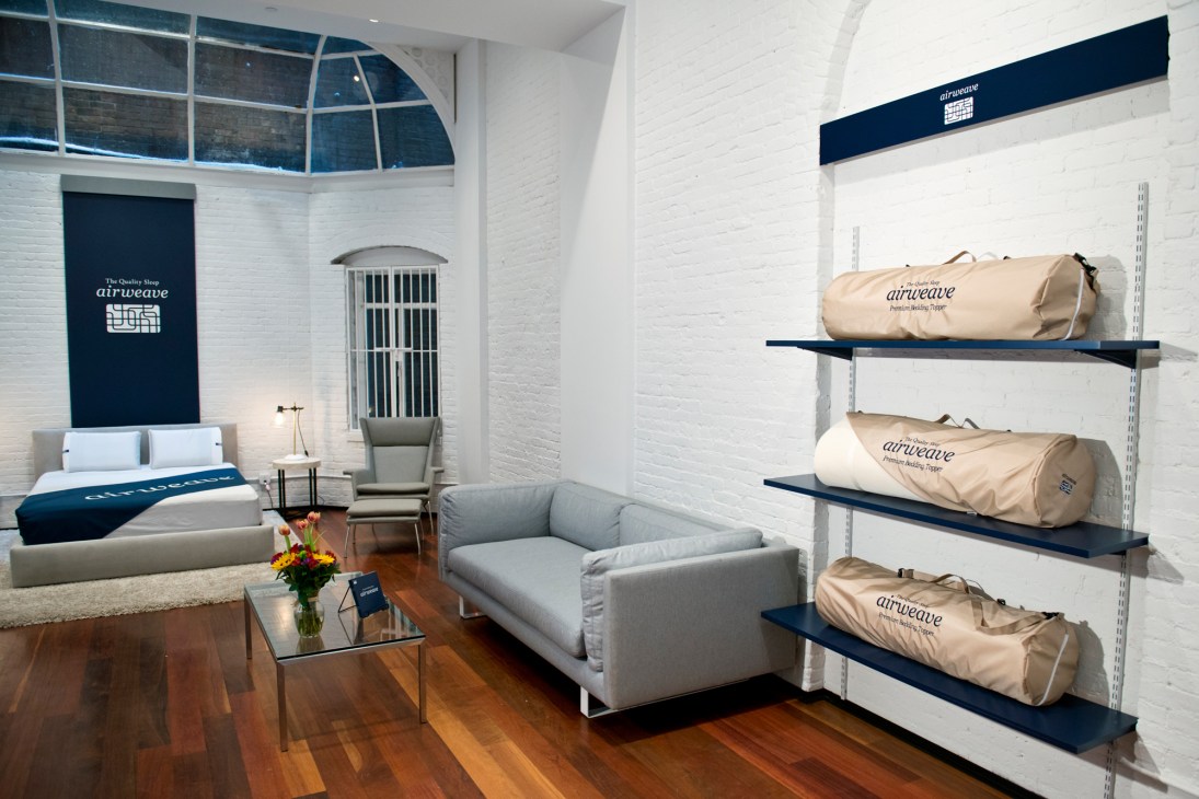 Airweave mattress store interior with display bed, chair, and packaged mattresses on shelves.