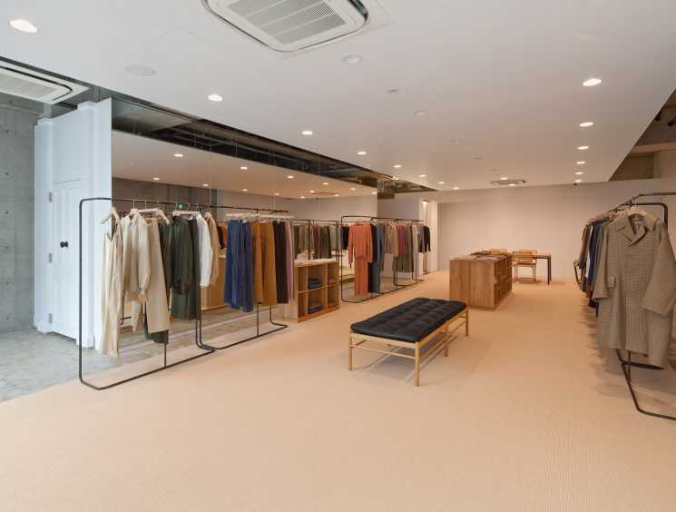Auralee flagship store interior in Tokyo's Aoyama neighbourhood with clothing on minimal iron racks and mid-century furniture.