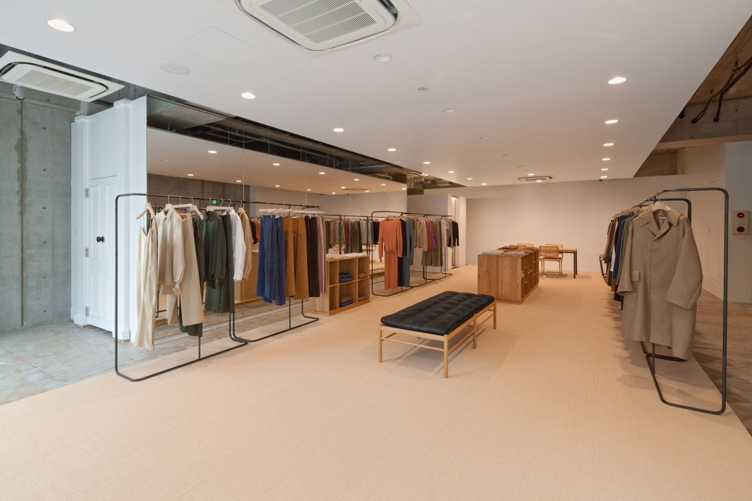 Minimalist retail interior with clothing on metal racks and wooden display fixtures by architect Nobuo Araki.