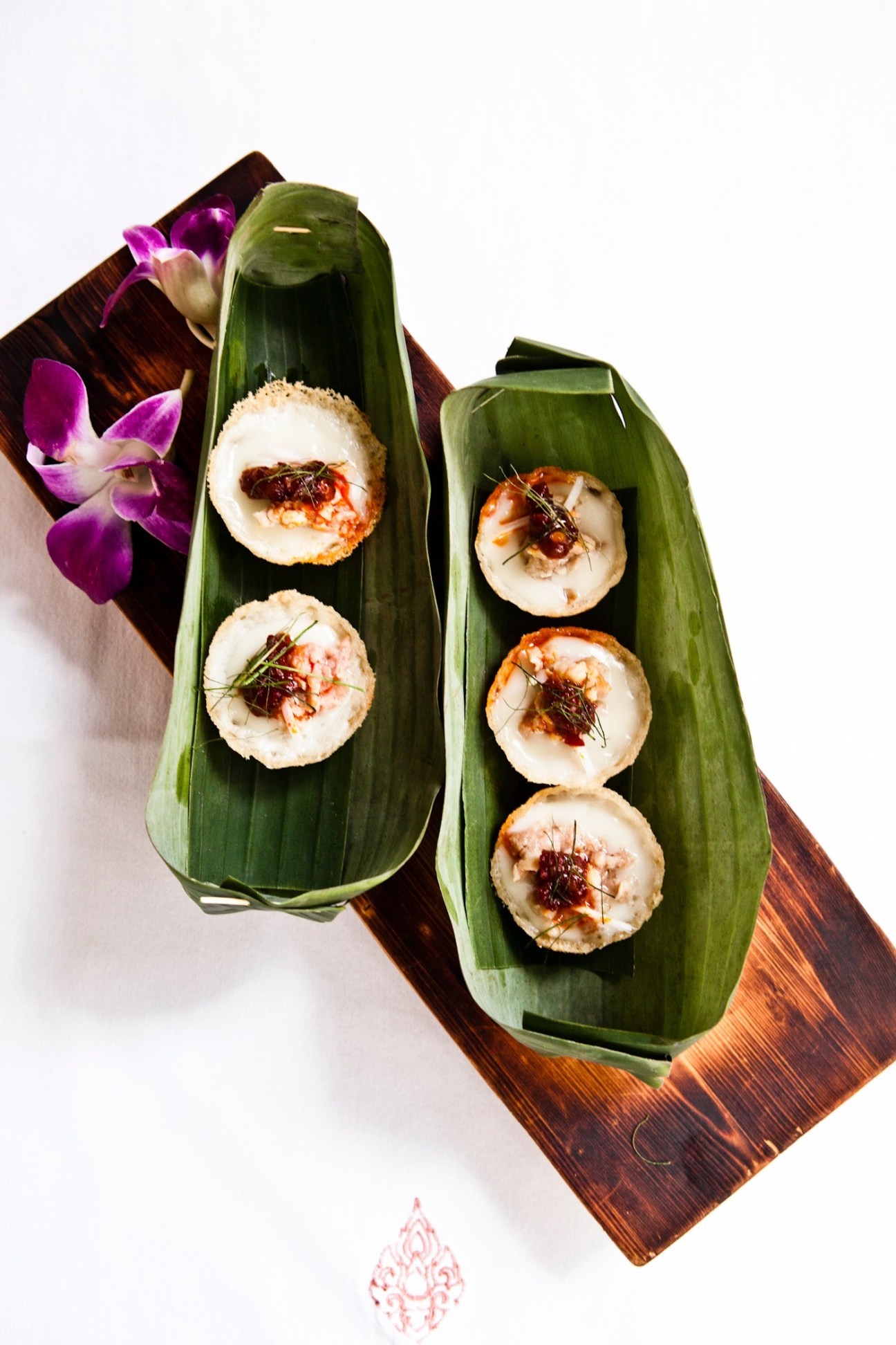 Thai coconut crème brûlée filled with chicken and kaffir lime leaf served on banana leaves with orchid flowers.
