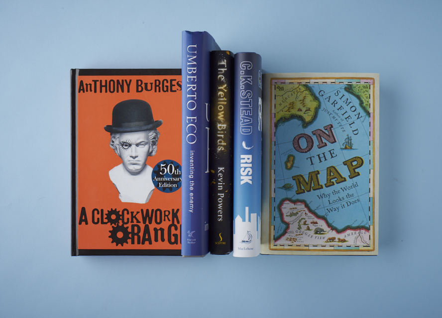 A selection of books displayed against a light blue background, including A Clockwork Orange, Umberto Eco's Inventing the Enemy, and Simon Garfield's On the Map.