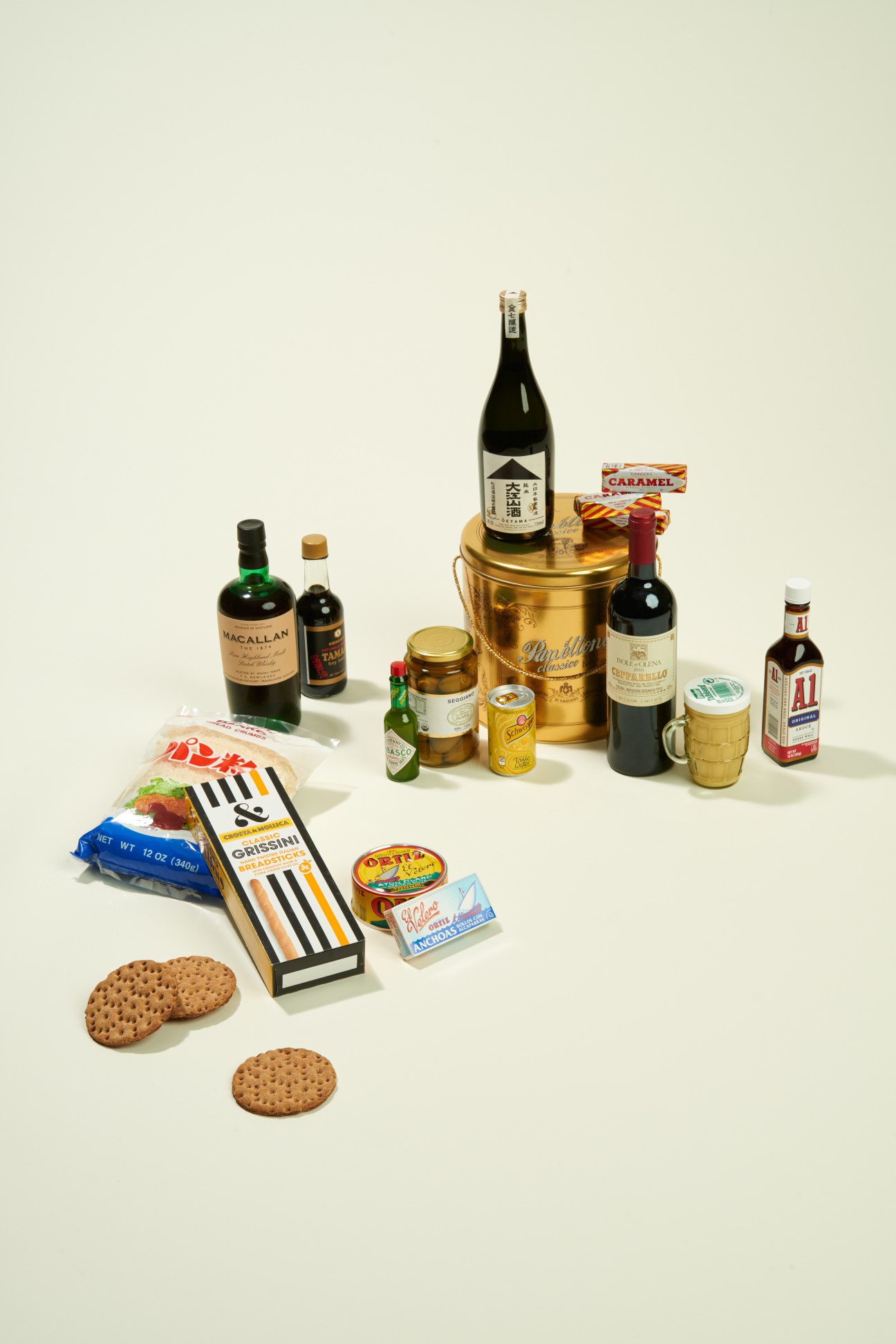 Curated selection of gourmet pantry items including wines, spirits, sauces, crackers, and preserved foods arranged on a neutral background.