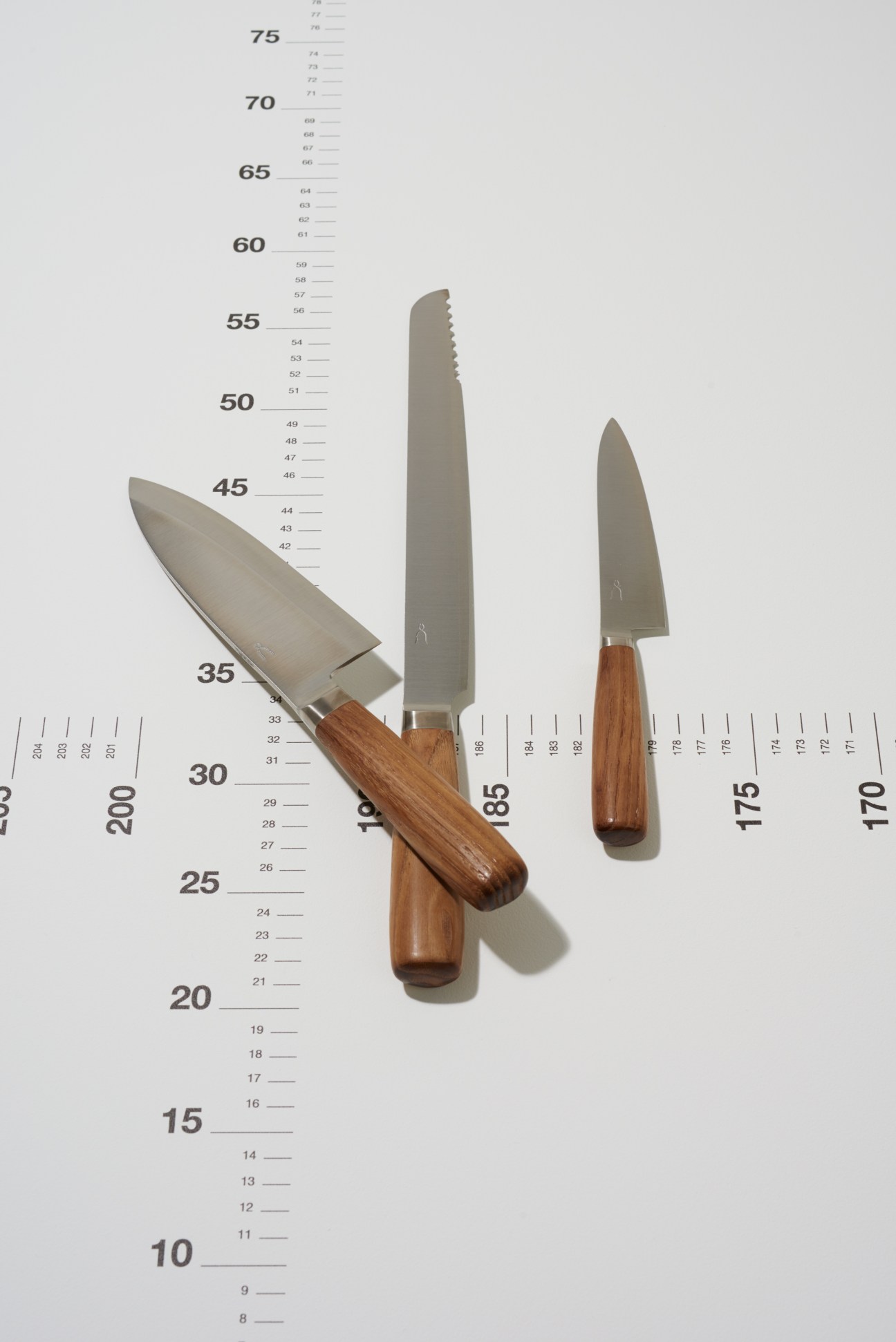 Three kitchen knives with smoked-chestnut handles displayed on a measurement scale.