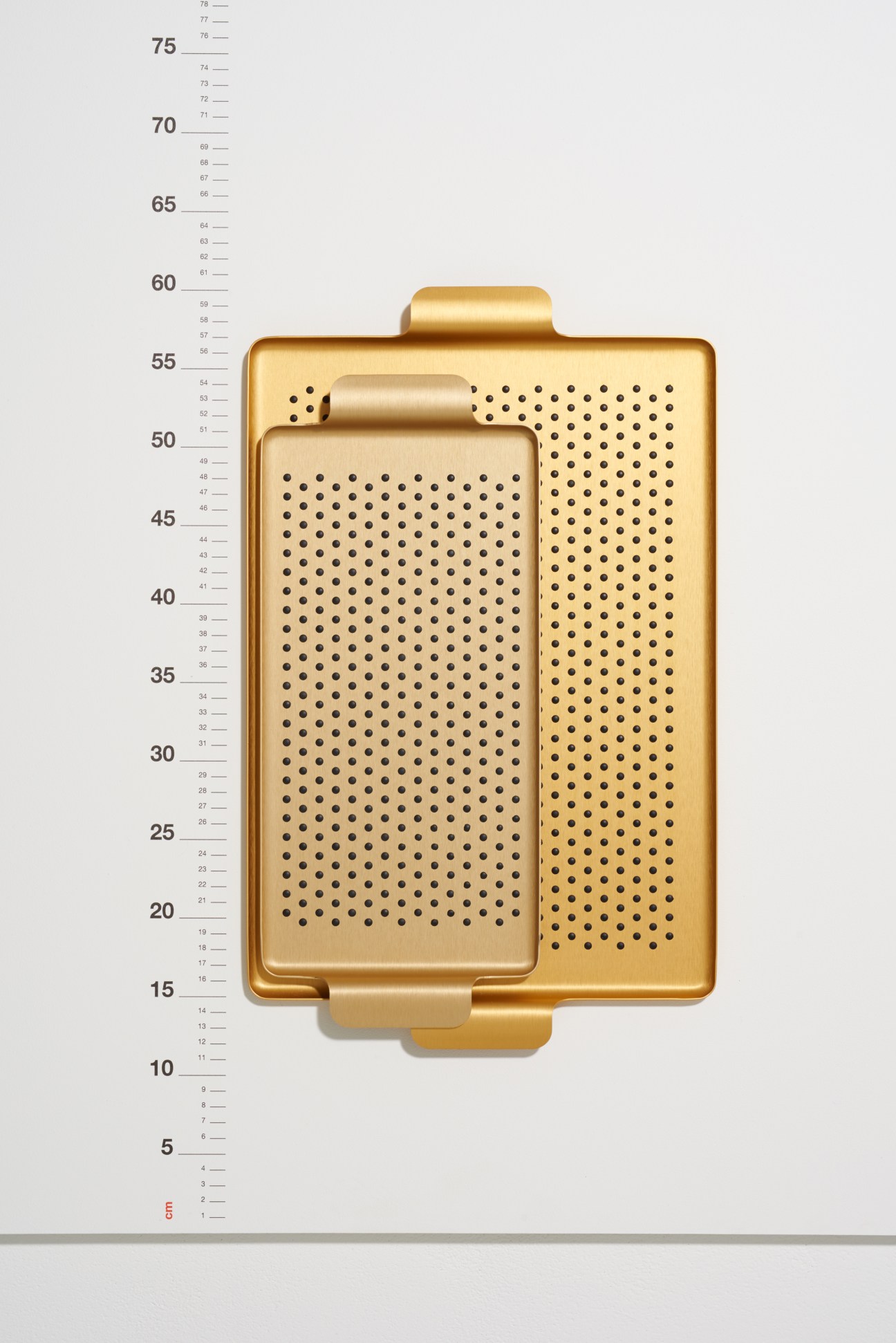 Gold-coloured aluminium trays with rubber studs by Kaymet, displayed against a measurement scale.