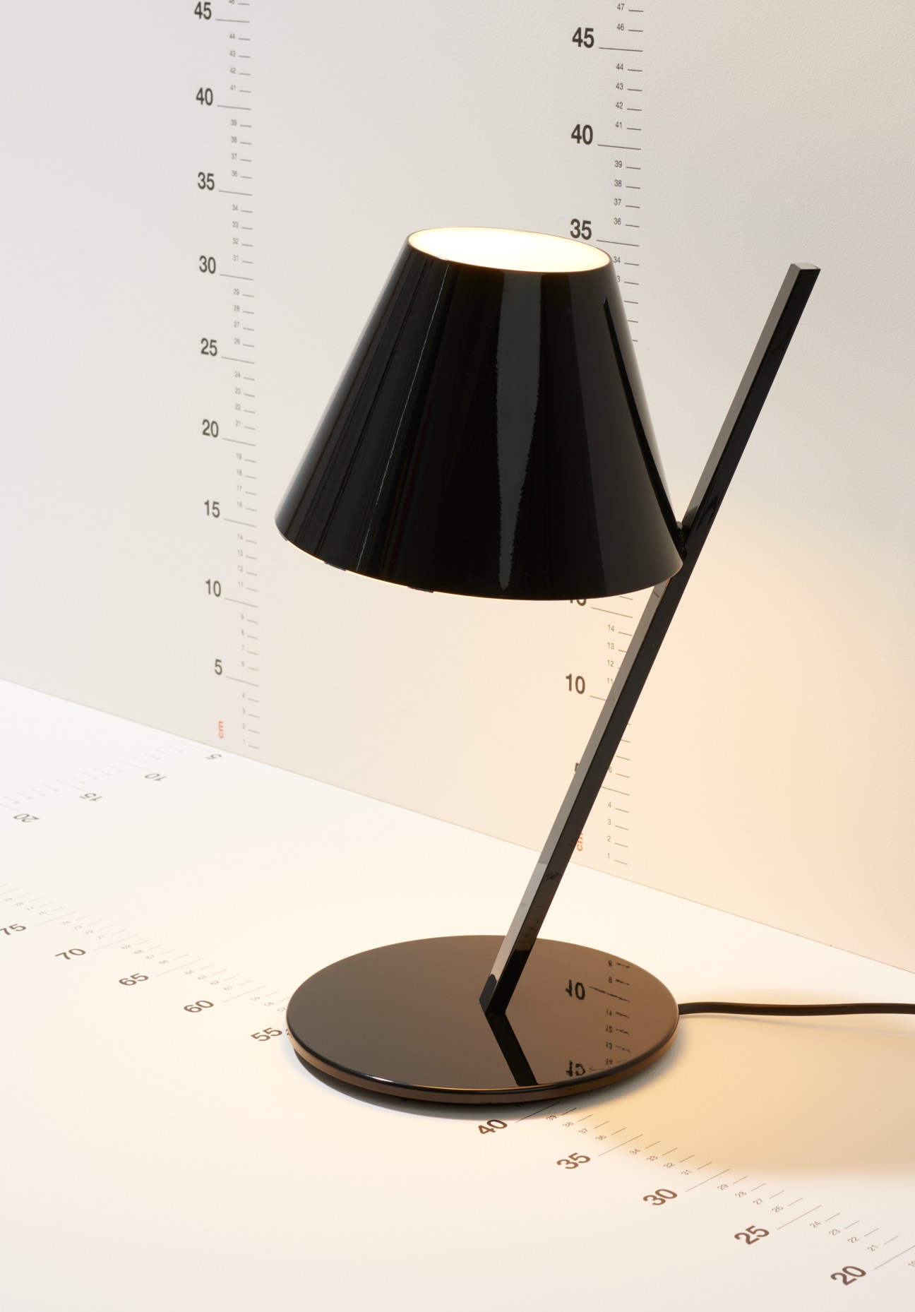 Black desk lamp with conical shade and adjustable arm on round base with measurement scale.