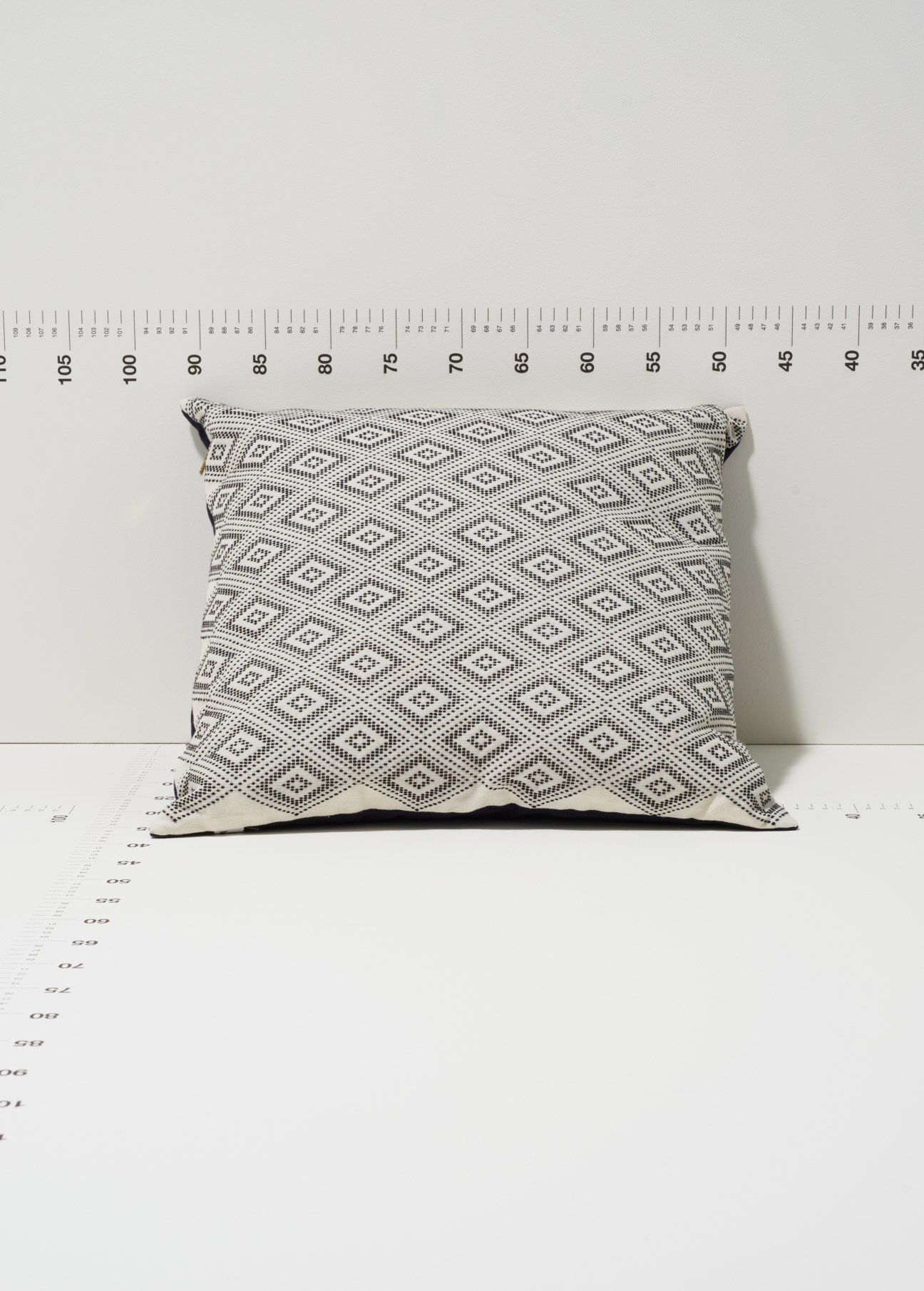 Bococo Bantay cushion with handwoven cream and charcoal diamond pattern displayed on measurement scale.