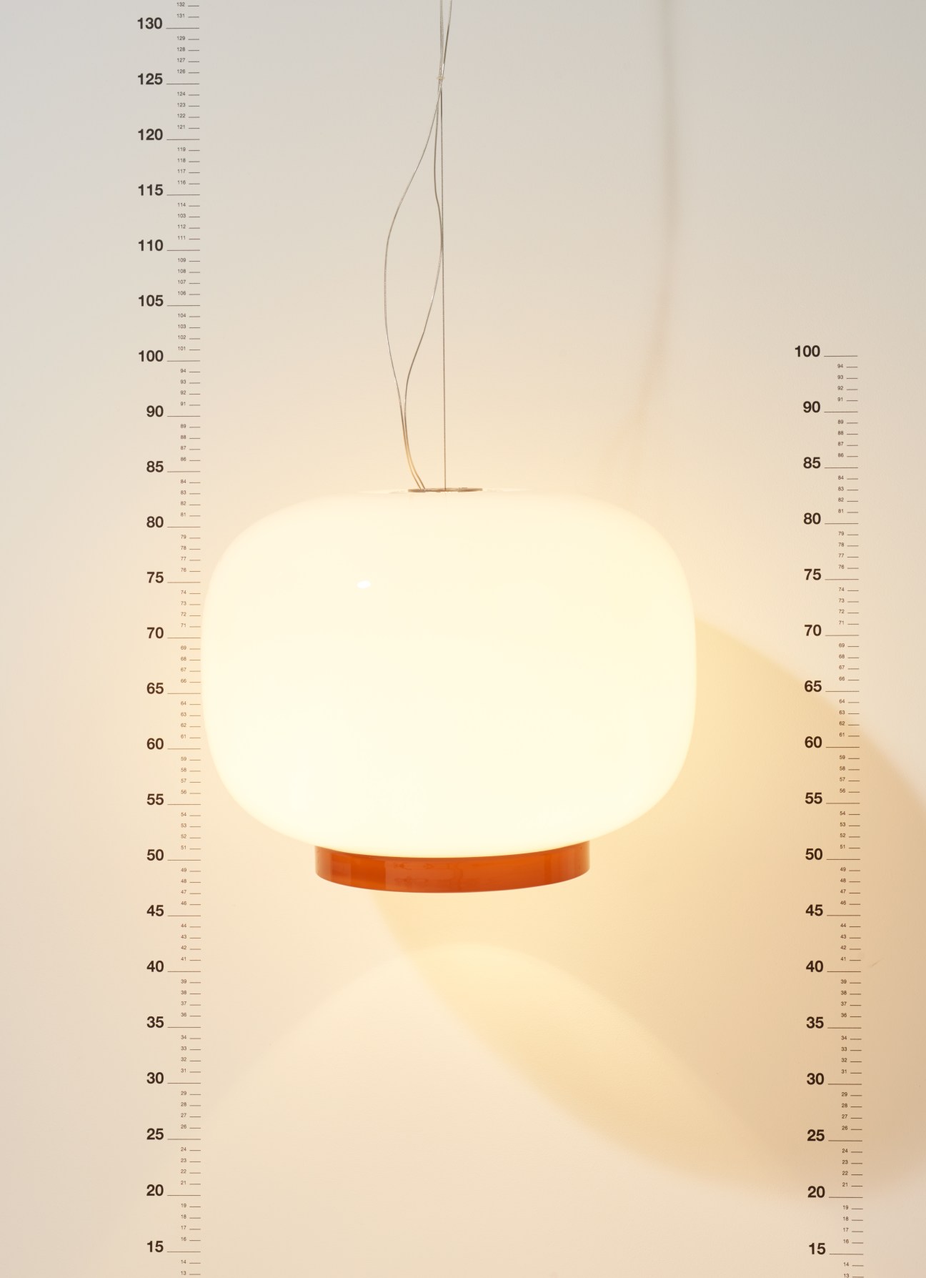 Chouchin Reverse lamp by Foscarini with blown glass globe and thin metal stem against measurement scale.