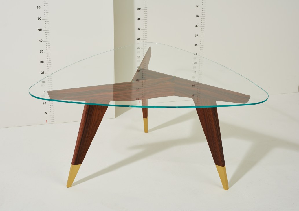 Mid-century modern table with walnut base, glass top, and brass geometric crisscross support structure.