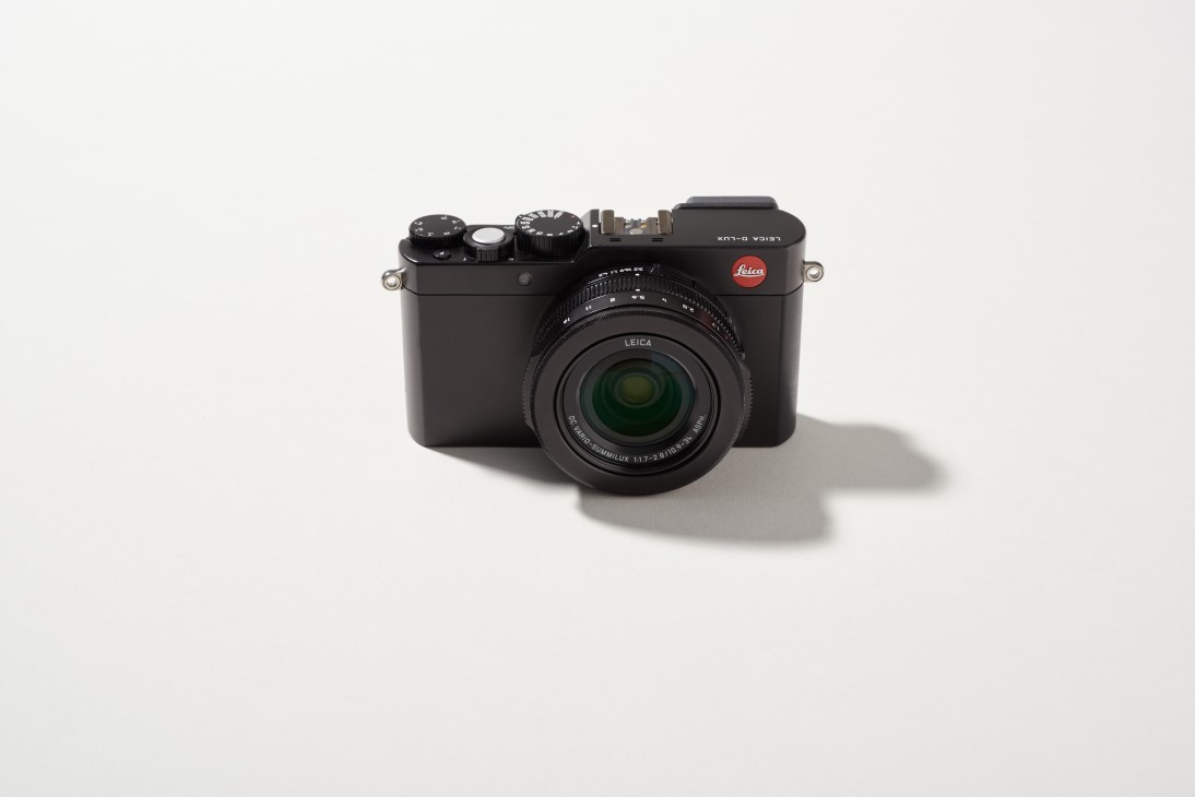 Leica D-Lux compact camera with black body and green lens element on white background.