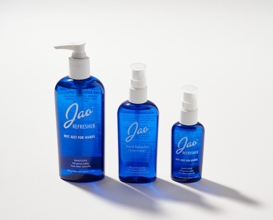 Three blue glass bottles of Jao Refresher hand sanitizer in different sizes with white pumps and spray tops.