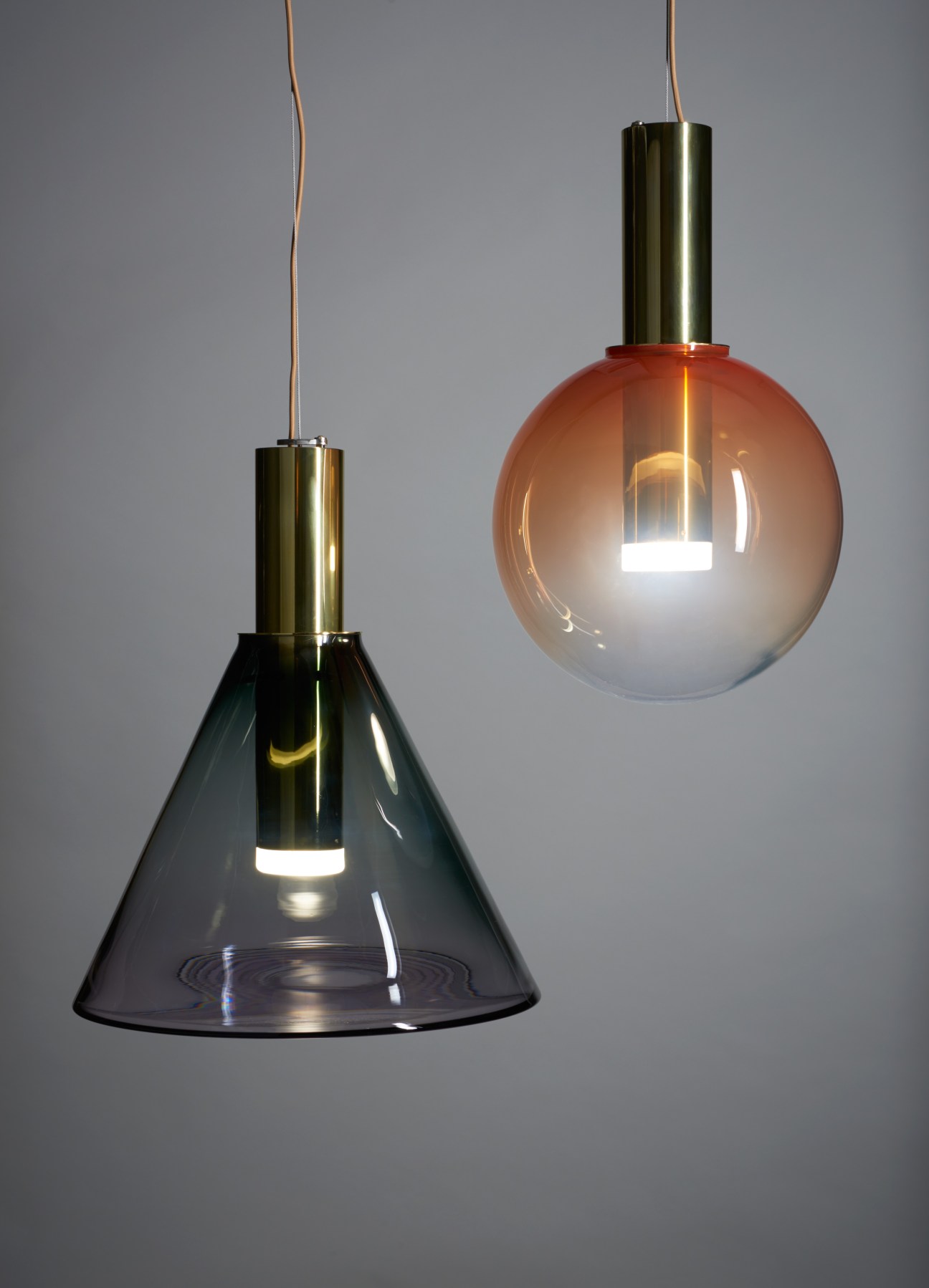 Two pendant lights with colored glass shades and brass fittings hanging against a gray background