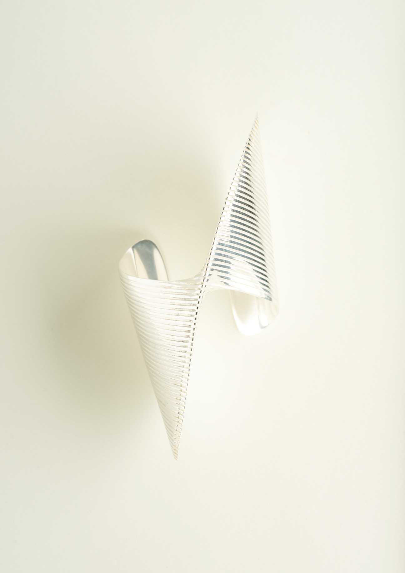 Silver bangle bracelet with fluid curved lines against a neutral background.