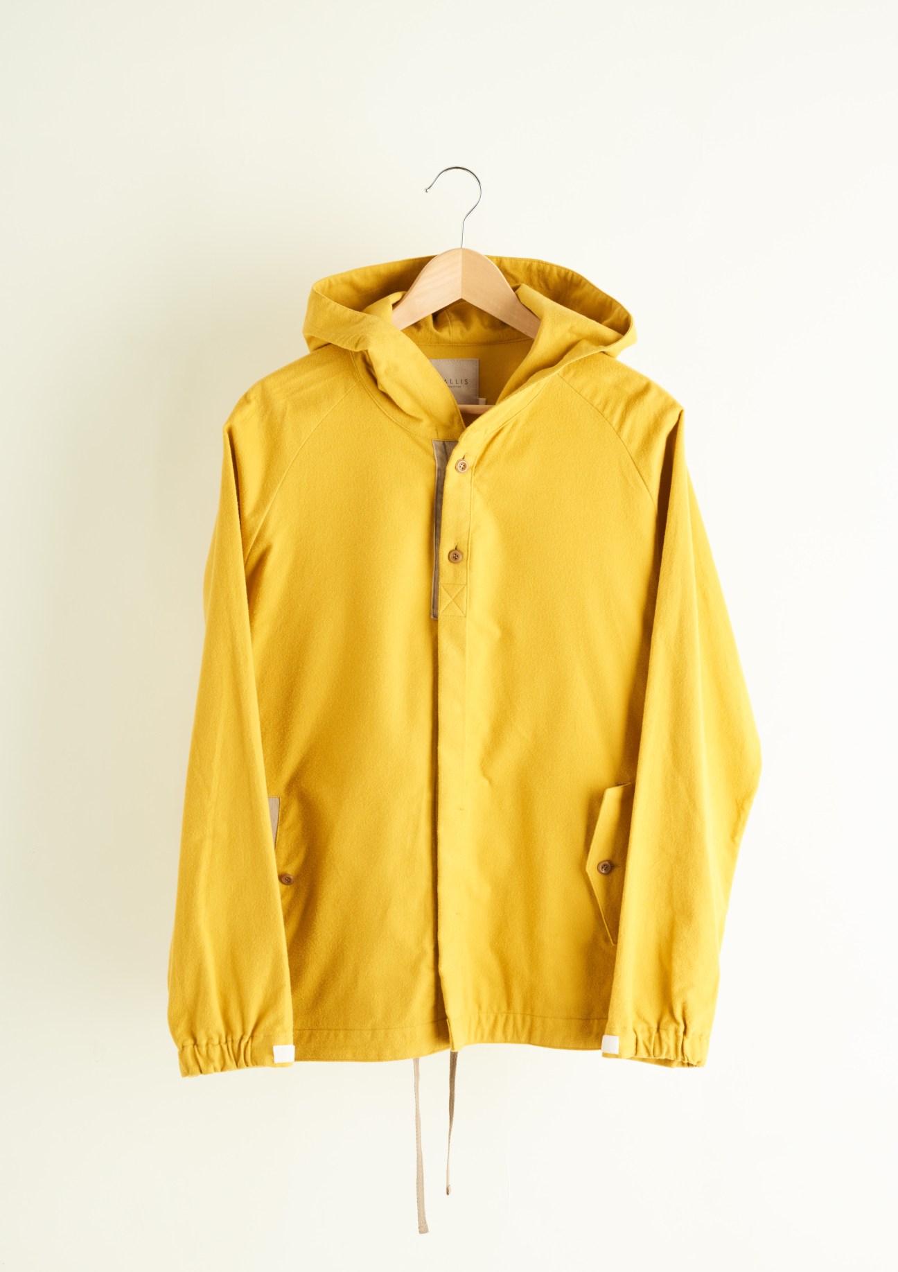 Mustard-hued flannel hooded jacket by Vallis by Factotum on wooden hanger against cream background.