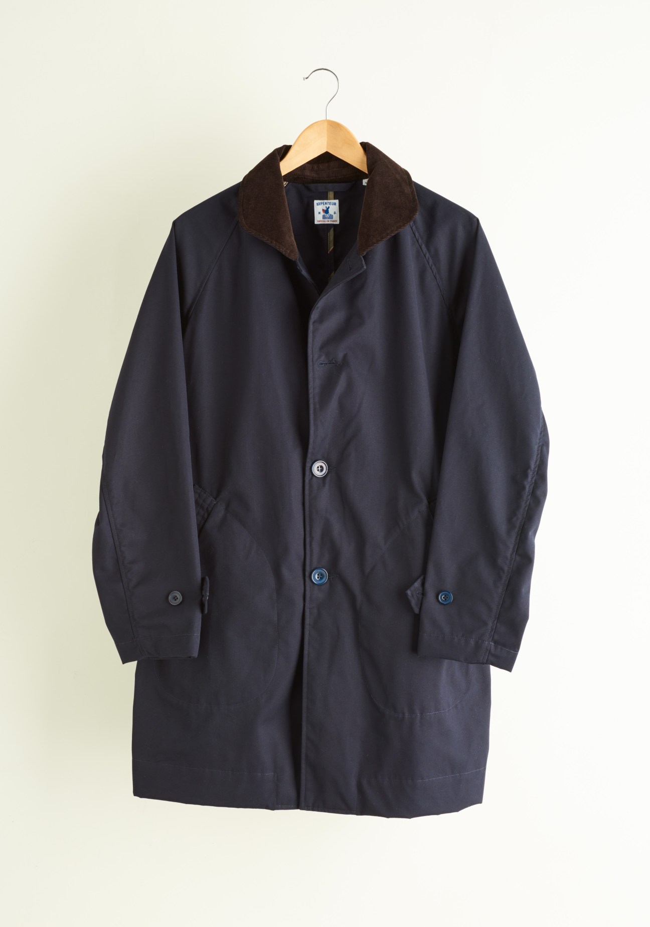 Navy corduroy-collared coat by Arpenteur x Drake's on wooden hanger against cream background.