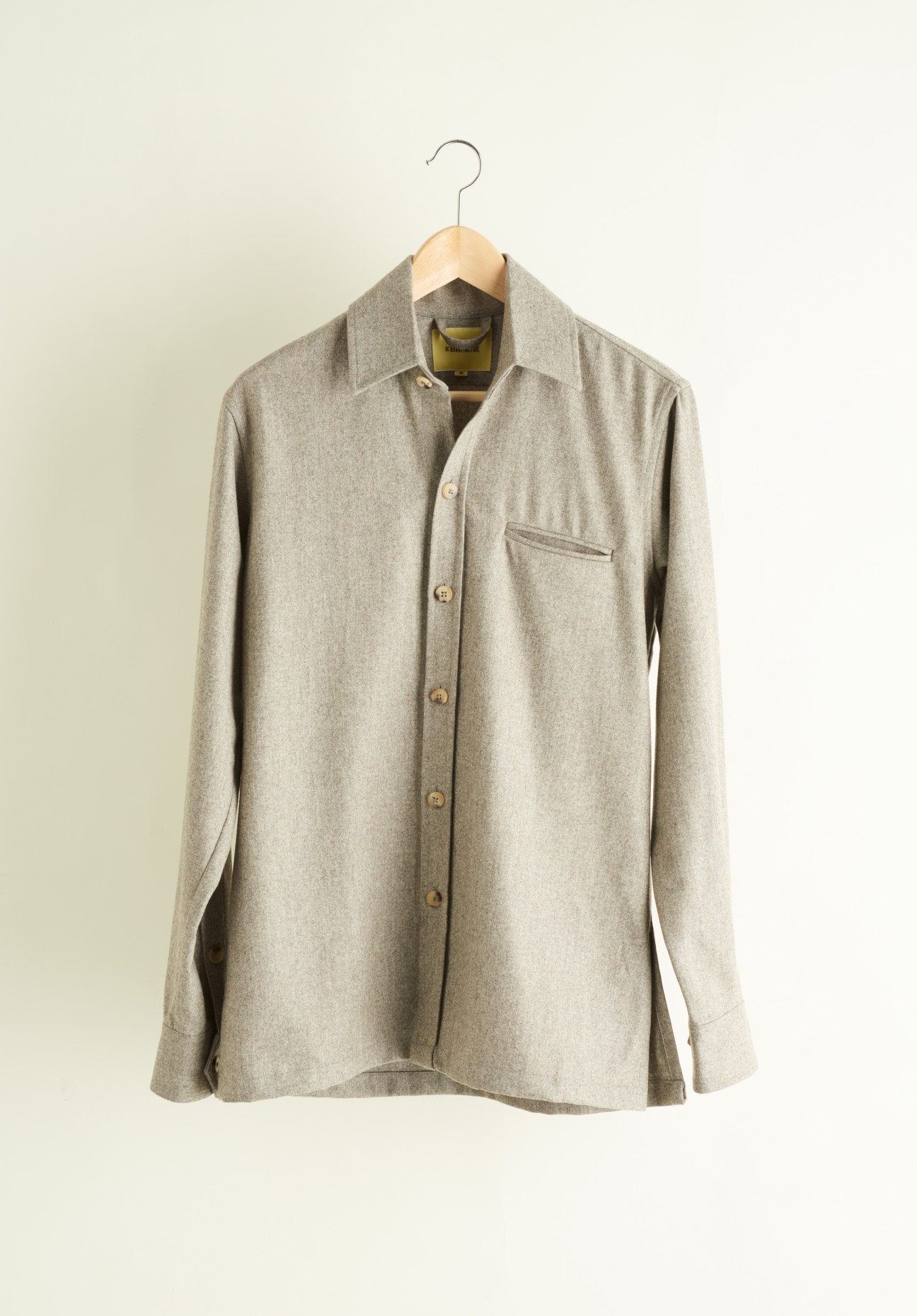 Beige linen shirt on wooden hanger against cream background.
