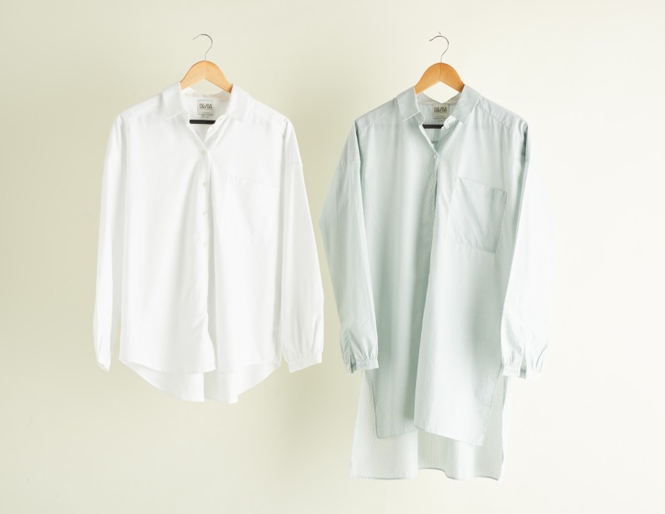 Two menswear-inspired shirts on wooden hangers: one white button-up and one sage green tunic-style shirt.