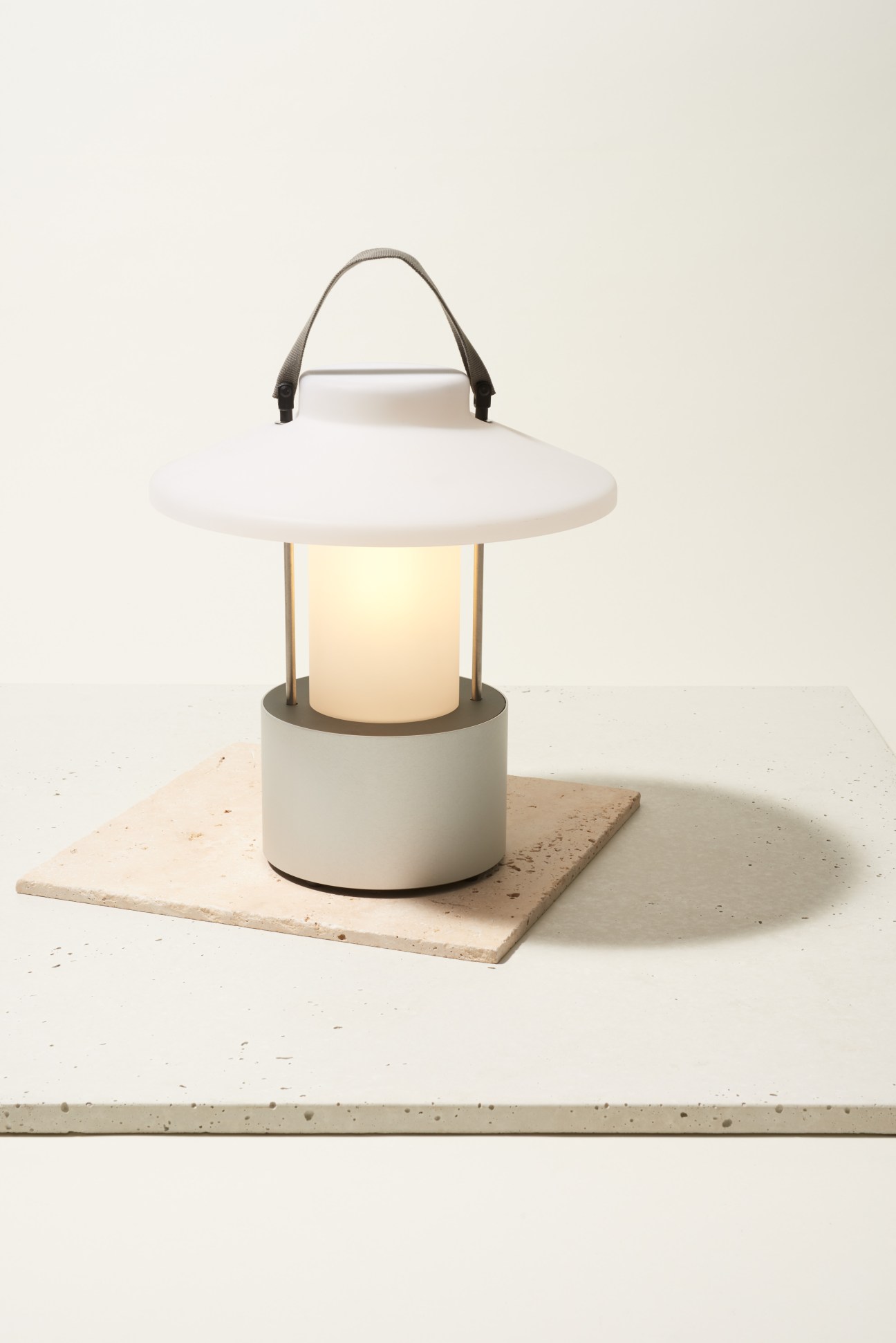 Trade Winds cordless outdoor lantern with white diffuser, metal handle and base on stone platform.